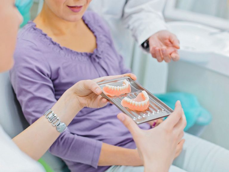 a dentist is showing sample of a dentures to a patient